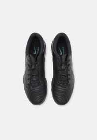 Black athletic shoes with a textured upper, featuring a wavy design. Laces are black, and there’s a subtle green logo on the tongue.