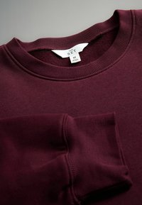 Burgundowy sweatshirt z okrągłym dekoltem, długimi rękawami i małą kieszonką na piersi. Metka mówi "THE SET", rozmiar M. Miękka struktura.