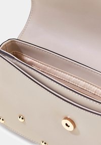 Intérieur de sac à main en cuir beige avec une texture lisse, des accents de quincaillerie dorée, une poche zippée et des détails de couture contrastés.