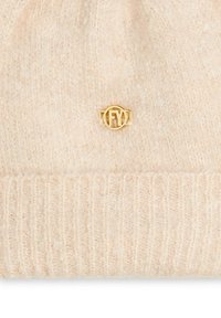 Tissu tricoté beige doux avec une texture côtelée en bas et un petit emblème rond doré avec les lettres "FY" au centre.