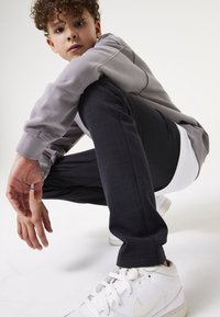 Grijze sweatshirt met geribbelde manchetten, zwarte textuur broek met een ruitpatroon, en witte sneakers met veters, tegen een neutrale achtergrond.