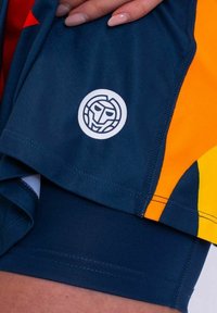 Pantalones cortos deportivos azul marino con acentos amarillos y naranjas. Presenta un logo circular blanco con una cara estilizada. Material suave, diseño ajustado.