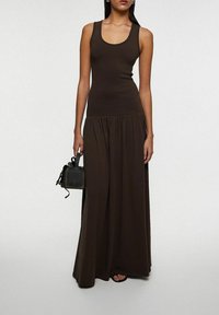 Brun tanktop parret med en flydende brun maxi-nederdel; outfittet har en glat tekstur og en fitted bodice med en samlet talje-detail.