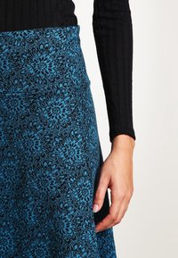 Falda de estampado floral con un patrón azul sobre un fondo negro, hecha de una tela texturizada, con una cintura ajustada y forma acampanada.