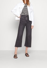 Svarta vida jeans med hög midja, kombinerat med en vit denimjacka och en svartvit randig skjorta. Sandaler med remmar i svart fulländar looken.