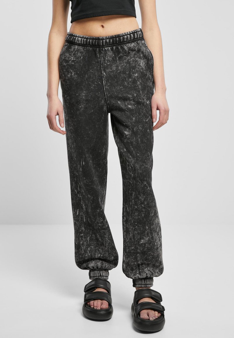 Sorte joggebukser med en myk, teksturert overflate, med elastisk midje og samlede mansjetter. Kombinert med tykke sorte sandaler.