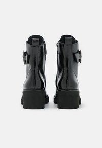 Bottines en cuir verni noir avec un talon bloc, dotées de zips latéraux et de boucles décoratives sur les côtés extérieurs. Texture lisse.