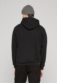 Felpa nera con collo e fascia in vita a coste, dotata di cappuccio con coulisse e maniche raglan. Indossata con pantaloni cargo scuri.