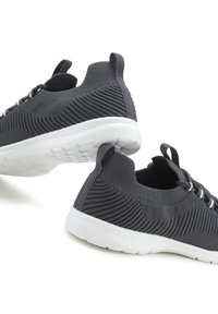 Zwarte sportieve schoenen met een textuur van gebreid bovenwerk, witte zool, ronde neus en contrasterende witte veters. Heeft een trekband aan de achterkant.