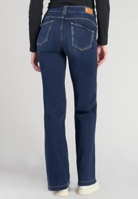 Pantalones vaqueros de mezclilla azul con un diseño de pierna recta, que cuentan con cinco bolsillos, costuras sutiles y una etiqueta de marca en la parte trasera de la cintura.