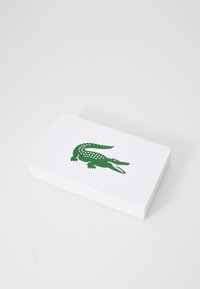 Cutie alb rectangular cu un logo de crocodil verde, suprafață texturată, cu solzi detaliați și un design cu gura larg deschisă.