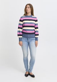 Pull rayé rose, bleu marine et crème, avec un col et des poignets côtelés. Associé à un jean skinny bleu clair et des ballerines noires.