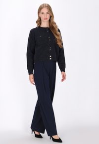Cardigan tricotat de culoare bleumarin, cu butoane aurii, asortat cu pantaloni bleumarin cu talie înaltă. Ţinuta are un material texturat şi o croială lejeră.