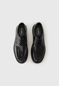 Black lace-up shoes featuring smooth leather, decorative silver studs along the sides, and a rubber sole with raised edges.