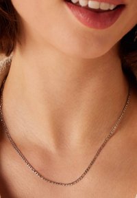Zilveren ketting met een verfijnd schakelontwerp, rustend op een gladde hals. Subtiele glans op het metaal, minimalistische esthetiek.