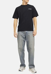 T-shirt nera in cotone con maniche corte, con la scritta "PARADISE" in bianco. Abbinata a jeans chiari a vestibilità ampia e sneaker grigie.