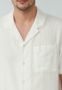 Witte short-sleeve shirt van textuurstof, met een ingesneden kraag, knopenluiting en een voorzak.