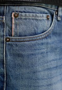 Džíny z denimu světle modré barvy s vybledlou texturou, viditelnými stehy a malou přední kapsou s červeným akcentem a kovovými nýty.