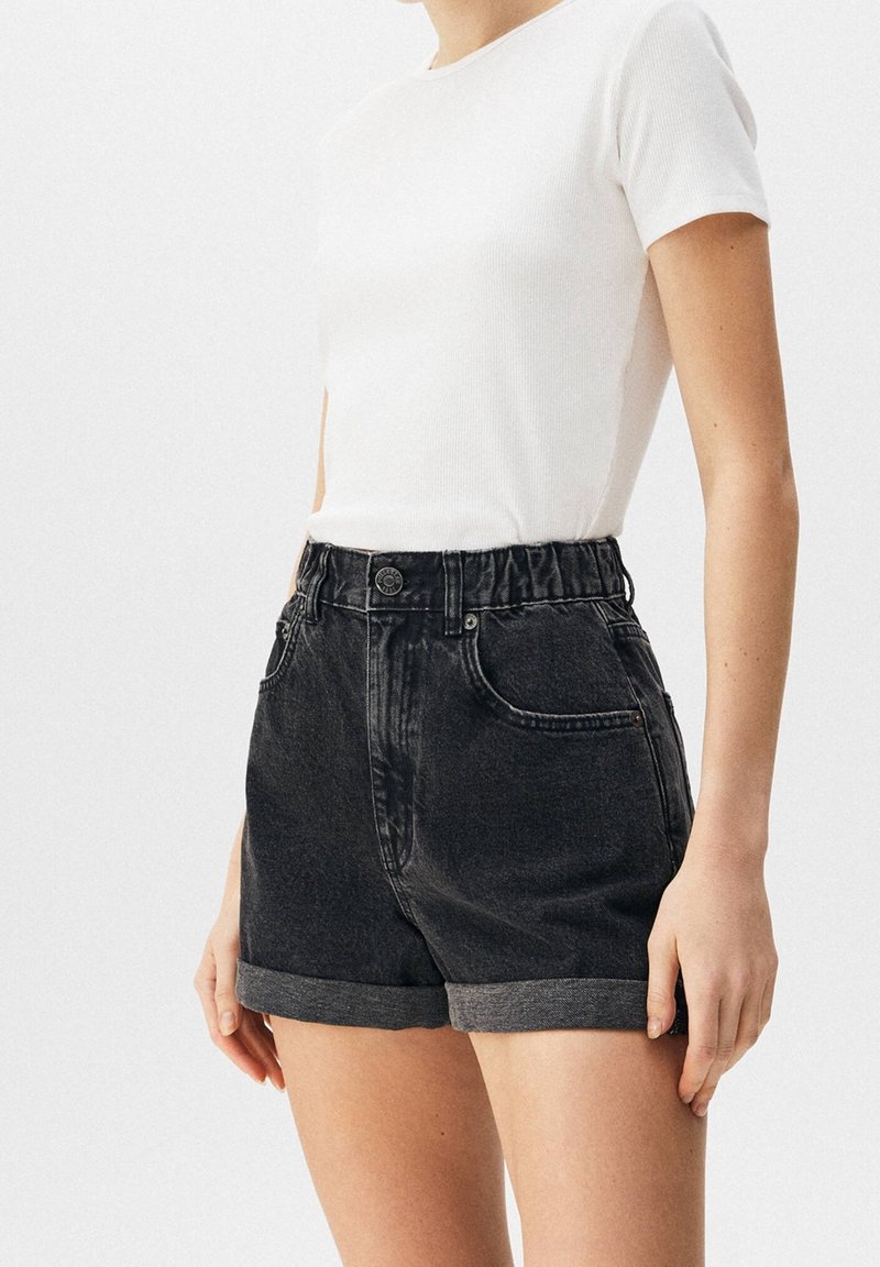 Mustat denimit sortsit, joissa on korkea vyötärö, käännetyt hihat ja sivutaskut. Valmistettu teksturoidusta kankaasta, jossa on nappi- ja vetoketjukiinnitys.