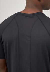 T-shirt de sport noir à manches courtes avec une texture lisse, présentant des panneaux en maille contrastants et des coutures renforcées au niveau des épaules et du dos.