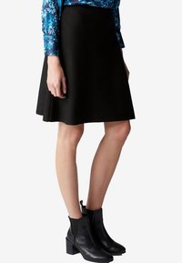 Gonna nera a ruota realizzata in un tessuto testurizzato, abbinata a stivali neri alla caviglia. La parte superiore presenta un motivo floreale blu.