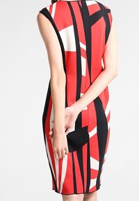 Vestido ceñido sin mangas en rojo, negro y blanco con un patrón geométrico. Tejido suave con un escote redondo y un largo hasta la rodilla.