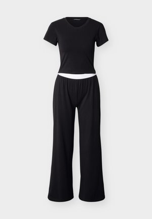 Černý dvoudílný outfit sestávající z krátkého trička s výstřihem do V a širokých kalhot s elastickým páskem a kontrastním bílým proužkem.