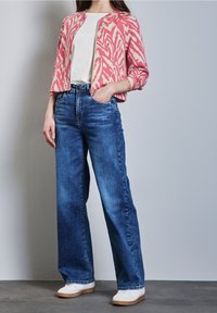 Färgglad stickad jacka i rosa och kräm med mönster, vit skjorta och vida denimjeans med klassisk passform och ljus tvätt. Avslappnade vita sneakers.