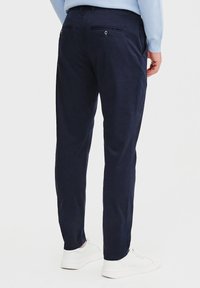 Granatowe spodnie o gładkiej fakturze, w wąskim kroju, z dwoma tylnymi kieszeniami zapinanymi na guziki. Stylizowane z białymi butami sportowymi.