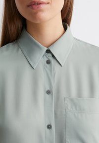 Light green collared shirt with a smooth texture, featuring gray buttons and a chest pocket, displayed without background distractions.
