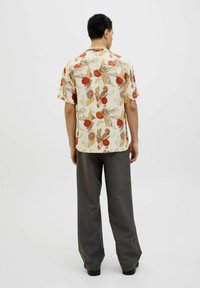 Cămașă cu mânecă scurtă, de culoare crem deschis, decorată cu un model abstract colorat, având accente roșii și verzi, combinată cu pantaloni largi gri.
