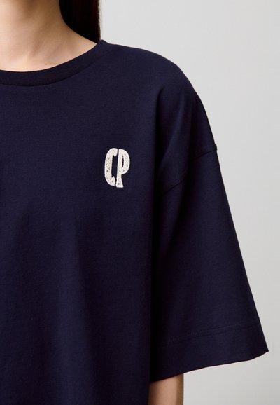 T-shirt en coton bleu marine avec une coupe décontractée. Présente un petit logo "CP" brodé en blanc sur la poitrine à gauche. Manches courtes.