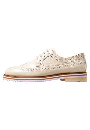 Beige læder blucher sko med detaljerede perforeringer, en rund tå, og en tofarvet stribet sål med en lav hæl. Lyse syninger som accent.