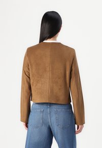 Brun ruskind cropped jakke med lange ærmer, der har en enkel rund halsudskæring og en glat tekstur, sammen med blå denimjeans.