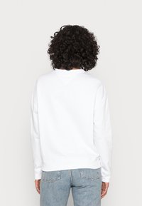 Felpa bianca con scollatura rotonda, polsini e orlo a coste. Presenta un design semplice e una consistenza morbida, vista da dietro.