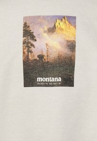 Camiseta de algodón gris claro con un gráfico rectangular de un paisaje montañoso con árboles, y el texto "montana" junto a las coordenadas debajo.