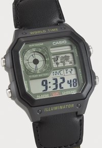 Montre numérique avec un boîtier carré noir, un affichage verdâtre, un bracelet en cuir et une étiquette de résistance à l'eau. Les fonctionnalités incluent l'heure mondiale et les réglages de l'alarme.