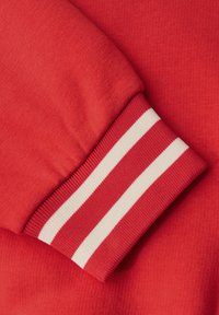 Rode sweatshirtmanchet gemaakt van gestructureerde stof, met witte horizontale strepen. De manchet sluit strak aan en heeft een geribbelde structuur.