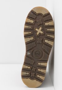 Semelle de chaussure marron avec un motif de bande de roulement texturé profond, taille 37, et logo circulaire portant l'inscription "Natural Life & Style" sur une surface blanche.