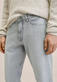 Jeans in denim azzurro chiaro con vestibilità dritta, dotati di chiusura frontale con bottoni e zip, e tasche laterali. Abbinati a un maglione a maglia strutturata.