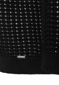 Schwarzer Strickpullover mit offenem Strickmuster, geripptem Saum und einem kleinen gewebten Etikett mit der Aufschrift "MORE & MORE" am unteren Rand.