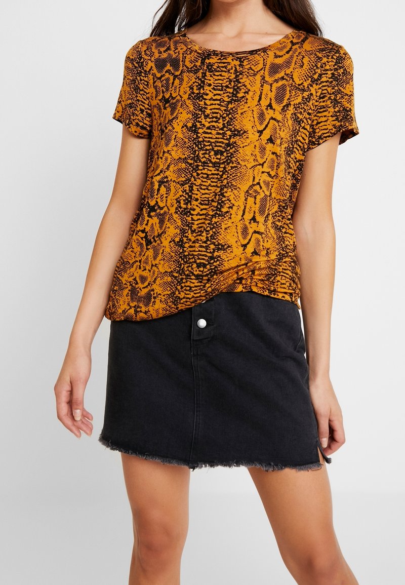 Koszulka z krótkim rękawem w pomarańczowy i czarny wzór w węża, w połączeniu z czarną spódnicą dżinsową z poszarpanym dołem i zapięciem na zatrzask.