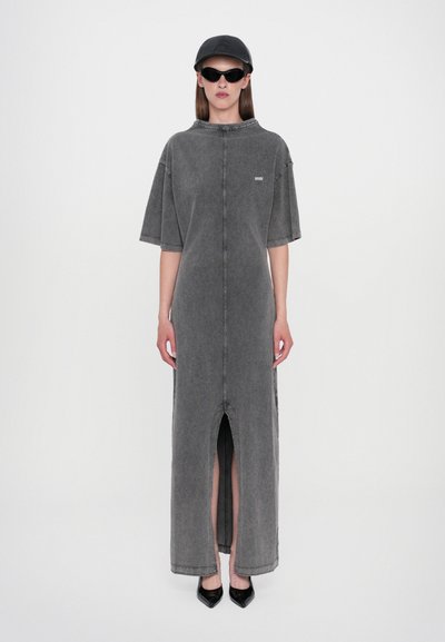 Grauer Jeans-Maxi-Kleid mit kurzen Ärmeln, das einen frontalen Schlitz und Nahtdetails aufweist. Getragen mit schwarzen Sonnenbrillen und einer Kappe, ergänzt durch schwarze High Heels.