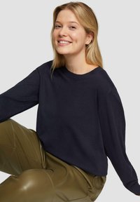 Navyblauwe sweater met lange mouwen en een ronde hals, gemaakt van zachte stof, gecombineerd met glanzende olijfgroene broeken. Minimalistisch ontwerp, geen patronen.