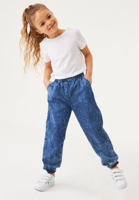 Vit t-shirt med kort ärm i kombination med blå denim-joggers med elastisk midja och ribbade ärmslut, komplett med vita sneakers.