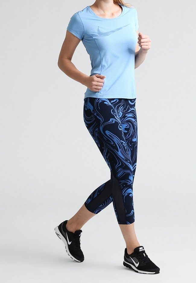 Top azul claro ajustado de manga corta combinado con leggings azul marino con un patrón azul en espiral. Zapatillas deportivas negras con suelas blancas.