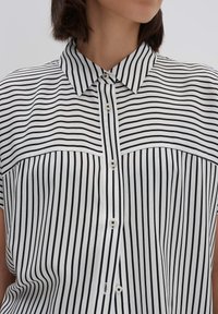 Camicia con colletto, a bottoni, bianca e nera a righe verticali. Presenta maniche corte e un tessuto leggero e morbido.