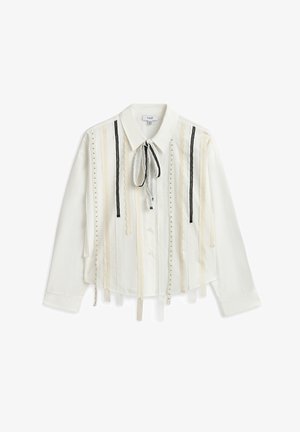 Camicia bianca con bottoni, caratterizzata da righe verticali di pizzo e nastri di tessuto, rifinita con un colletto a fiocco e maniche a sbuffo.