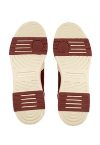 Sarkani zamšādas sporta apavi ar baltiem gumijas zoleņiem, kas izceļas ar horizontālām rieviņām un apaļu logotipu uz papēža. Līdzenas zoles ikdienas valkāšanai.