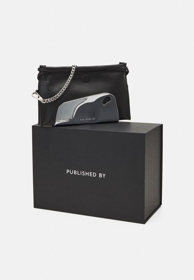 Black leather pouch with a silver chain strap, paired with a metallic object and a matte black box featuring white text that reads "PUBLISHED BY."